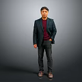 Man Standing in Dark Blazer Red Sweater Black Pants Against Gray Background Hands in Pockets