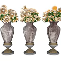 Three Metallic Vases With Decorative Bases Holding White And Beige Flowers With Green Leaves