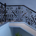 Ornate Staircase With Black Iron Railings Blue Wall Green Plant Black Vases And Pebble Decor