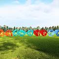 Colorful Circular Sculptures Displayed on Green Grassland With Woodland and Blue Sky Background