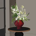 Red Glazed Vase with White Blooms and Greenery on Round Wooden Table in Interior