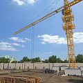 Construction Site With Tower Crane Blue Sky White Clouds Wooden Planks Bricks And Green Trees