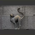 Bronze Cat Sculpture With Curled Tail Standing Against Rustic Stone Wall