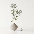 White Ceramic Vase With Green Leaves And Small White Flowers On Minimalist White Table