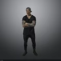 Tattooed Man Wearing Black T Shirt And Pants With Arms Crossed Against Gray Background