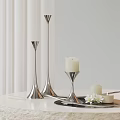 Silver Candle Holders Featuring White Lit Candle Small Candle and White Flowers on Light Tabletop