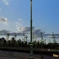 Outdoor Street Lamp Under Blue Sky With Clouds Trees Railings And Distant Buildings