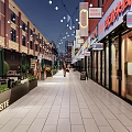 Vibrant Commercial Street With Red Roof Buildings Shops Outdoor Seating Green Plants And String Lights