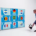 Young Boy Kicking Football Towards Soccer Goal With Numbered Panels And National Flags