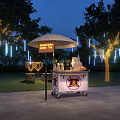 Mobile Coffee Bar Cart With Umbrella In Outdoor Night Setting Decorative Lights And Trees