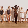 Group of women posing in swimsuits and towels against white wall with wooden floor