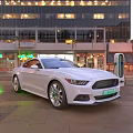 White Car At Electric Vehicle Charging Station In City