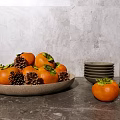 Fresh Persimmons in Brown Plate with Pine Cones Bowls and Clear Cups on Gray Tabletop