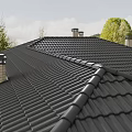 Black Roof Tiles And Chimneys On Residential Roof Structure With Green Trees Background