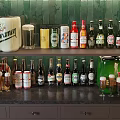 Various Brands of Beer Bottles And Beer Glasses On Black Countertop With Green Tiled Background