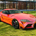 Orange Sleek Sports Car With Black Wheels Parked On Green Grass Outdoor