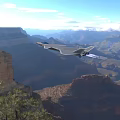 Gray Fighter Jet Flying Over Canyon With Mountainous Landscape And Trees