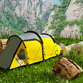 Yellow And Gray Camping Tent Set Up On Green Grassland With Mountain Rocks And Backpacks