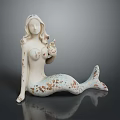 Mermaid Statue With White Body Brown Spots And Blue White Tail Sitting On Black Surface