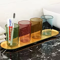 Daily Washing Essentials With Colorful Glass Cups Toothpaste Toothbrush And Green Leaves On Wooden Tray