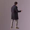 Man in dark coat gray pants brown shoes pointing to side with light brown background
