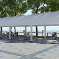 White Arched Columned Canopy with Electric Scooters Under Trees on Paved Ground