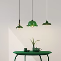 Green Pendant Lights With Floral Bell Shapes Above Green Table With Teapot And Plant