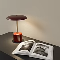 Red Base Metallic Stand Maroon Shade Table Lamp On Black Desk With Open Photo Book