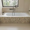 Stylish Bathtub with Stone Base and Black Faucet Near Window with Green Plants and Bottles