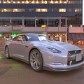 Silver Sports Car Parked on Urban Street with City Buildings and Illuminated Lights at Dusk