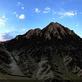 Scenic Mountain Landscape With Rolling Brownish Yellow Peaks Green Grass Blue Sky And White Clouds