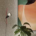 Floor lamp with silver head and red wire against gray wall near green plant