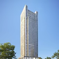 Modern Tall Office Building With Glass Curtain Wall Exterior Against Blue Sky And Green Trees