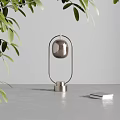 Stylish Table Lamp With Metal Frame And Glass Globe On Gray Tabletop With Green Leaves