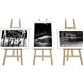 Art Supplies Display Featuring Three Wooden Easels With Black And White Landscape Paintings In Frames