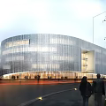 Modern Museum Building With Curved Exterior Design Glass Facade Lighting Effects And Surrounding Pedestrians Trees
