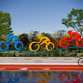Colorful Blue Yellow Red Bicycle Sculptures Near Track With Trees And Person Cycling