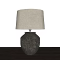 Beige Linen Lampshade Table Lamp With Textured Ceramic Base On Dark Wooden Tabletop