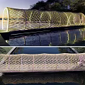 Illuminated Cylindrical Woven Landscape Bridge Over Pond With Reflection in Natural Surroundings