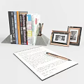 Stack of books magazines open notebook with handwritten notes stationery items and photo frames on desk