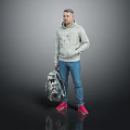 Man in Gray Hoodie Blue Jeans Red Shoes Holding Patterned Backpack Against Gray Black Background