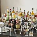 Assorted Alcohol Bottles and Drinking Glasses on Table with Cocktail Shakers and Ice Buckets