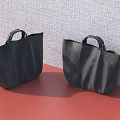 Two Black Leather Handheld Bags On Red Surface With Gray Textured Wall