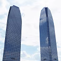 Two Tall Office Buildings With Glass Curtain Walls Against Blue Sky And White Clouds