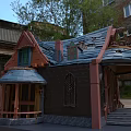 Cartoon Style House With Blue Tiled Roof Red Walls And Arched Windows Near Old Buildings And Trees