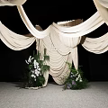 Stylish Floral Display Featuring White Draped Fabric And Central Decorative Greenery On Gray Floor