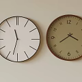 Two Wall Clocks With Minimalist And Numeral Designs Hanging On Beige Wall For Home Decor