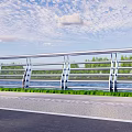 Metal Railing With Glass Panels Along Riverside Road And Green Vegetation