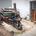 Motorcycle with cart parked near white wall and rusted door beside red flowers