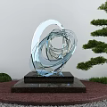 Transparent Glass Garden Sculpture With Twisted Circular Design Black Stone Base And Green Pine Tree 3d model